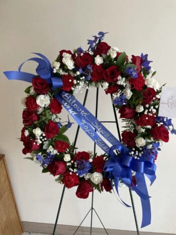 A wreath of red, white and blue flowers with a ribbon.